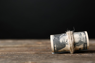 Dollars roll on wooden table in front of dark background