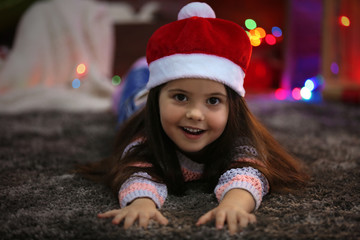 Pretty little girl in red hat laying in Christmas decorated room