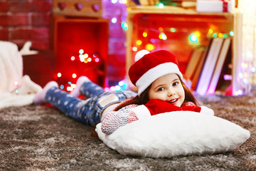 Pretty little girl in red hat laying on the pillow in Christmas decorated room