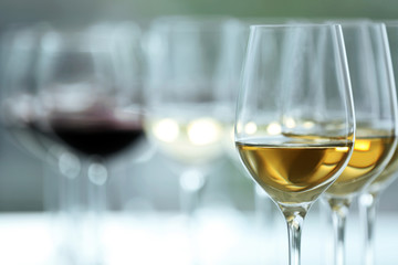 Wineglasses with white and red wine on wooden table on bright background