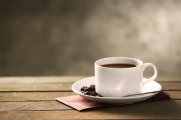 Cup of coffee and coffee grains on wooden table, on gray background