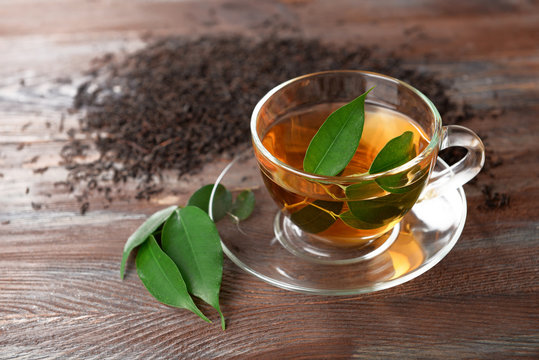 Glass cup of tea with green leaves on wooden background decorated with scattered tea
