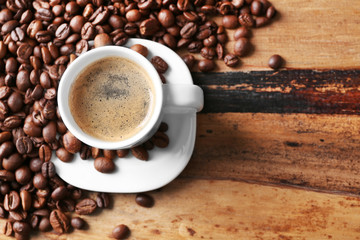 Cup of coffee and coffee grains on wooden table background