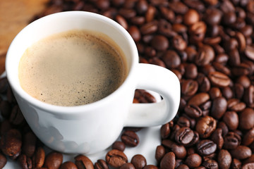 Cup of coffee and coffee grains on wooden table background
