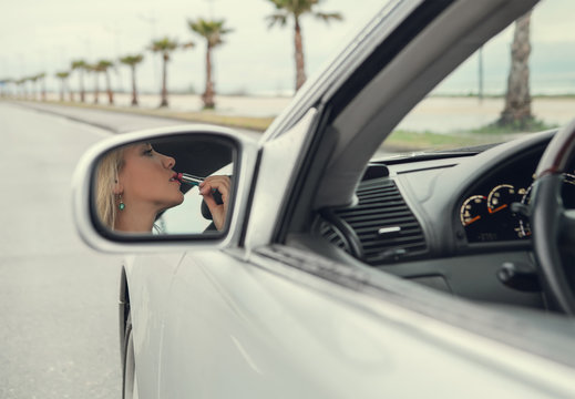 Woman apply  lipstick looking in rear view car mirror