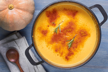 Pumpkin soup in pot on wooden table with wooden spoon, napkin and pumpkin.