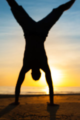 Blurred silhouette of young man making handstand on the beach.