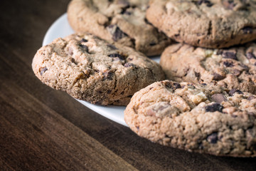 Several Chocolate Cookies Lying On The Edge Of A White Plate On A Wooden Vintage Table