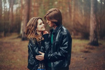 young happy loving couple in leather jackets hugs outdoor on cozy walk in forest