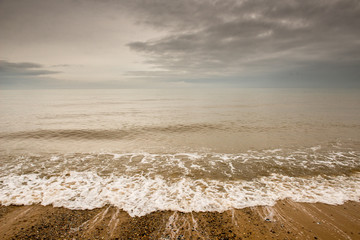Wave turning on to a stony beach and sky
