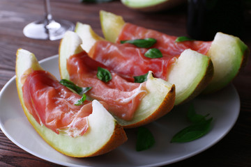 Melon with prosciutto of Parma ham on wooden table, closeup