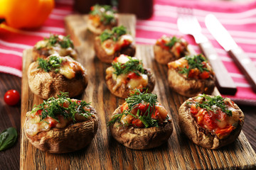 A wooden tablet with stuffed mushrooms and vegetables on the table
