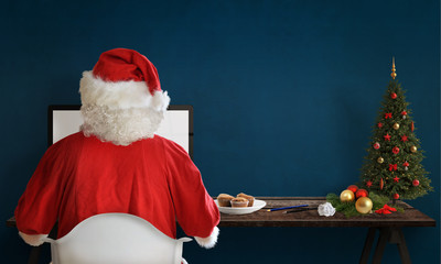 Santa Claus responds to letters on a computer for Christmas. Gifts, Christmas tree and decorations...