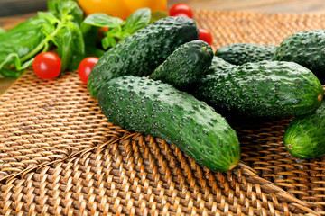Composition of cucumbers, tomatoes and sweet peppers on wicker serviette against wooden background