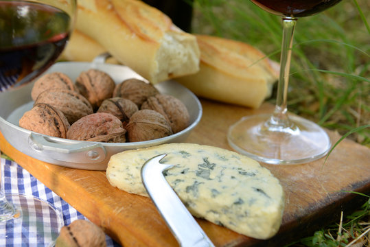 Picnic concept - Wine, delicious cheese, walnuts and baguette on wooden board, close up