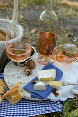 Picnic theme - rose wine, cheese, baguette and nuts outdoors, close up