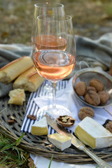 Picnic theme - rose wine, cheese, baguette and nuts on wicker tray, outdoors