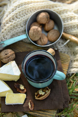 Mug with red wine, delicious cheese and nuts on wooden board outdoors - picnic theme