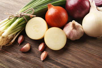 Fresh different onions with garlic on wooden background