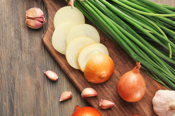 Fresh different onions with garlic on board against wooden background