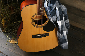 Fototapeta premium Acoustic guitar and blue checkered shirt against box with hay on wooden background, close up