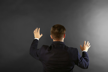 Back view of Caucasian young man in navy blue suit pointing on dark grey background