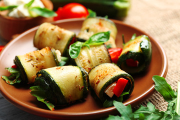 Salad with arugula and zucchini rolls on plate, on table background