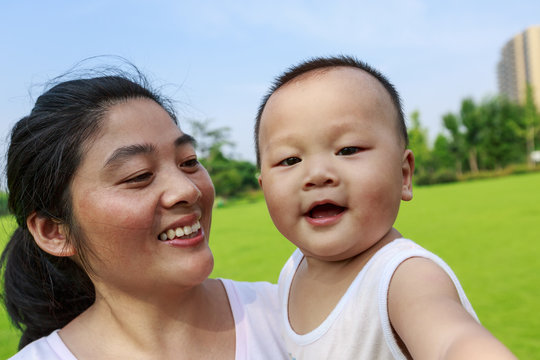 Happy Oriental mother holding baby playing on the grass
