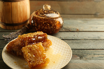 Honeycombs on plate, pot with honey and wooden barrel on wooden background