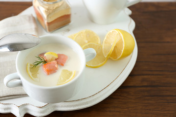 Delicious salmon cream soup with sliced lemon on white tray, close up