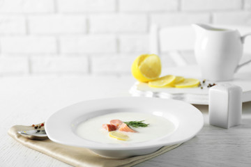 Delicious cream soup with fish and sliced lemon on white table in the restaurant