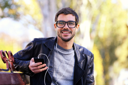 Young man sitting on a bench in park and listening to music