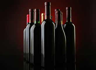 Wine bottles in a row on dark red background, close up