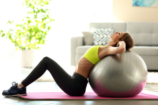 Beautiful young girl doing exercises with fit ball at home