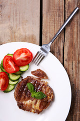 Roasted beef fillet and fresh vegetables on plate, on wooden background