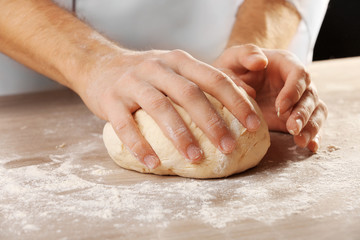 Hands kneading dough for pizza on the wooden table, close-up