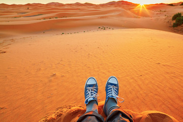 Woman relaxing on sand dunes and looking at sunrise in Sahara Desert