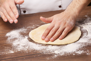 Obraz premium Hands preparing dough basis for pizza on the wooden table, close-up