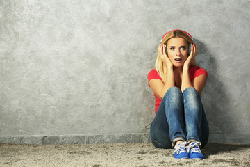 Young woman sitting on the floor and listening to music on a grey wall background