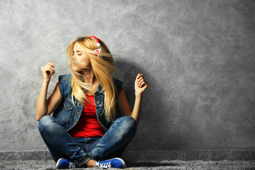Young woman sitting on the floor and listening to music on a grey wall background