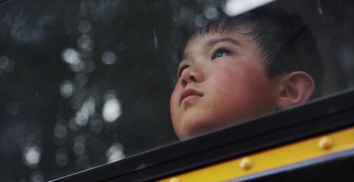 Young asian boy looking out the window of the school bus