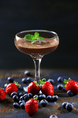 Chocolate dessert in glass and fresh berries on color wooden background