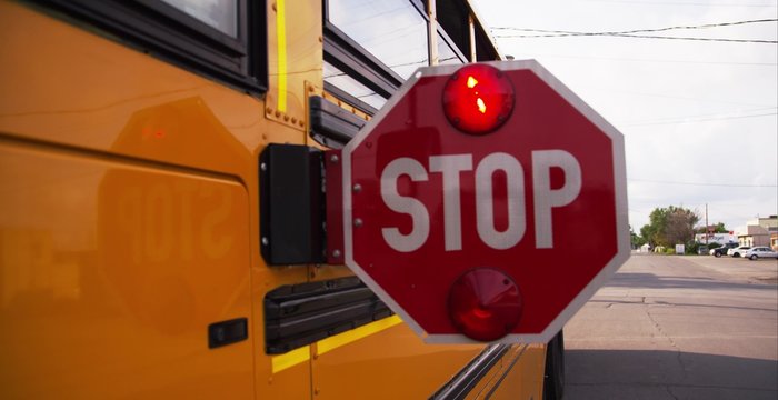 Stop sign on the side of a school bus telling traffic to wait for kids to cross