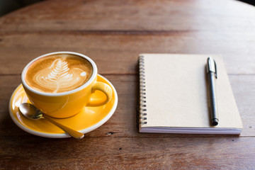 Hot latte art coffee cup on wooden table and note book.