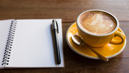 Hot latte art coffee cup on wooden table and note book.
