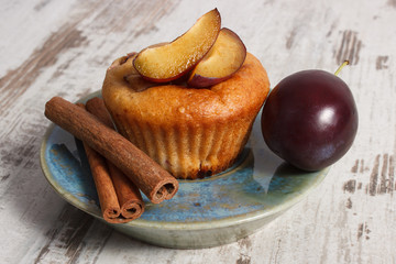 Fresh baked muffins with plums and cinnamon sticks on old wooden background, delicious dessert