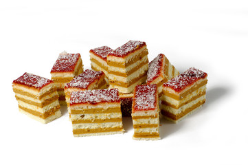 close-up of ten pieces of delicious layered sponge and custard cake, with red frosting and coconut sprinkles ontop, on a white background