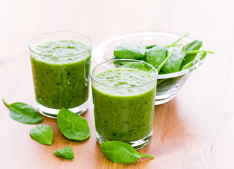 Two glass of green smoothie with spinach on wooden surface