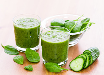 Two glass of green smoothie with spinach and cucumber on wooden surface