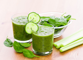 Two glass of green smoothie with spinach and celery on wooden surface, with slices of cucumber on the glass